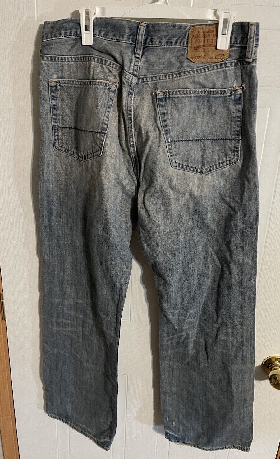 Abercrombie distressed bootcut jeans hanging on white hanger showing back pockets and label
