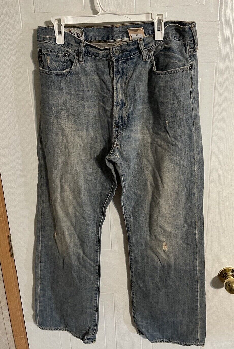 Abercrombie distressed bootcut jeans in faded blue denim hanging on a white door