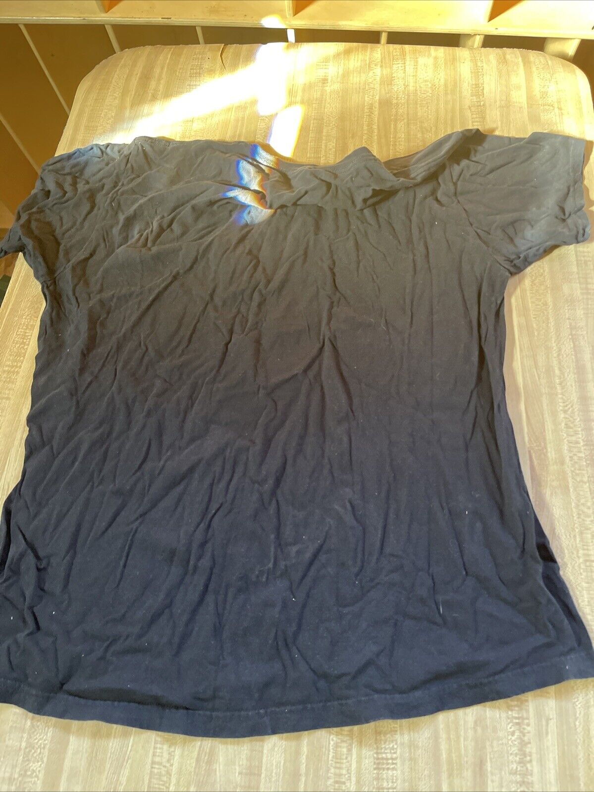 Black Aaliyah graphic t shirt laid flat on a bed with visible wrinkles and natural sunlight