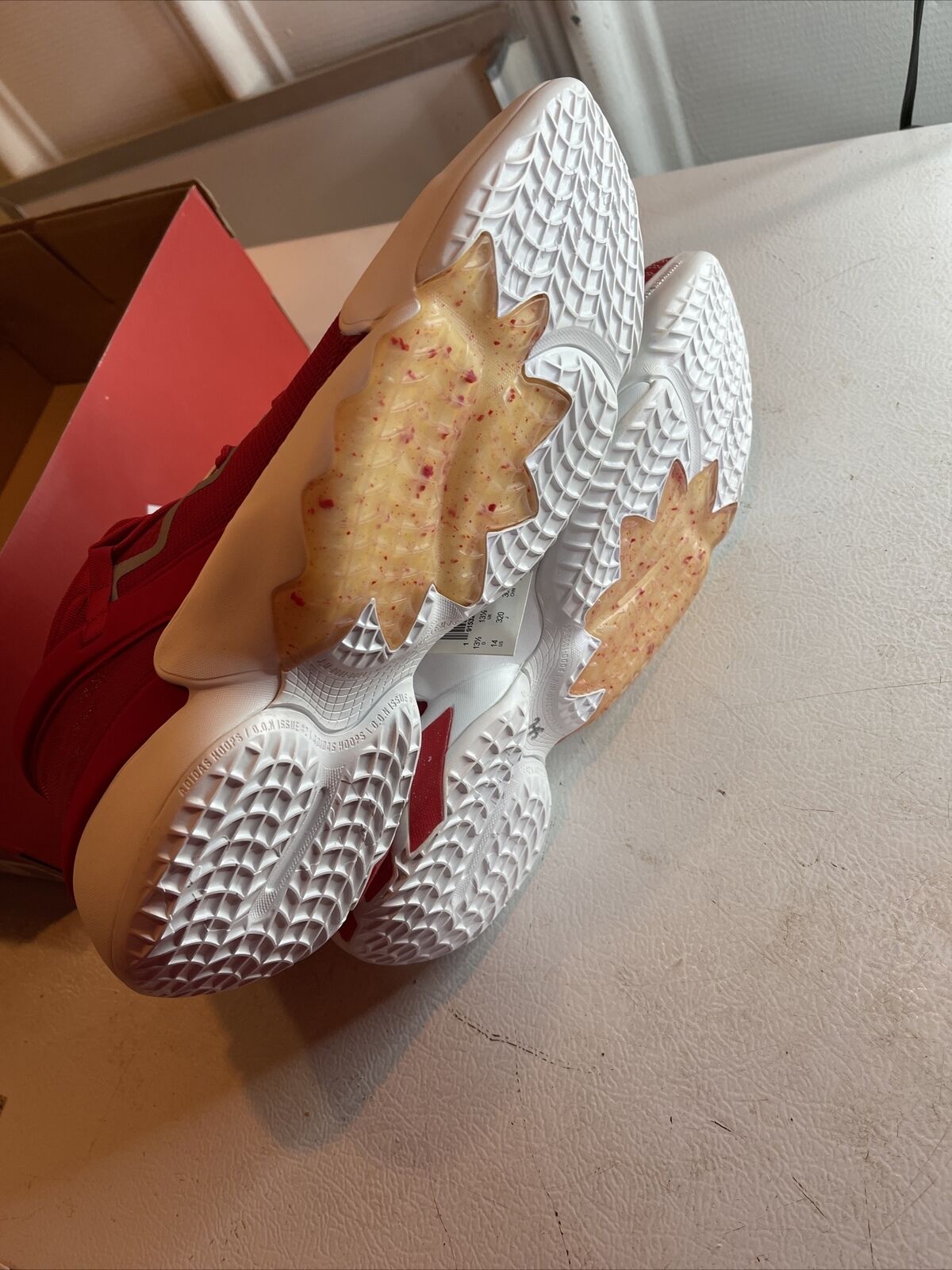 Men's red adidas basketball shoes showing white textured soles with grip pattern and beige midfoot support