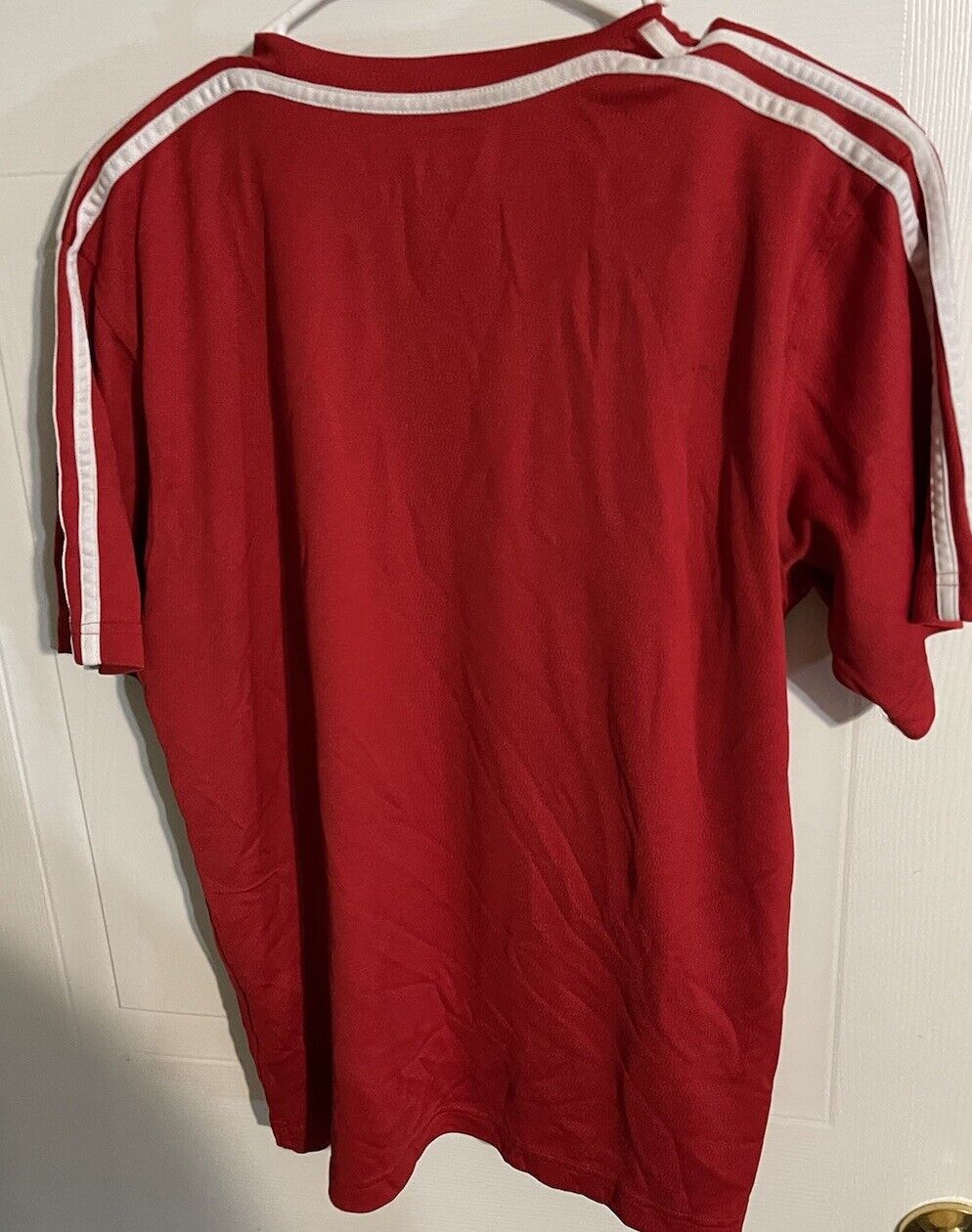 Adidas red t shirt small with white stripes on sleeves hanging on hanger against white door