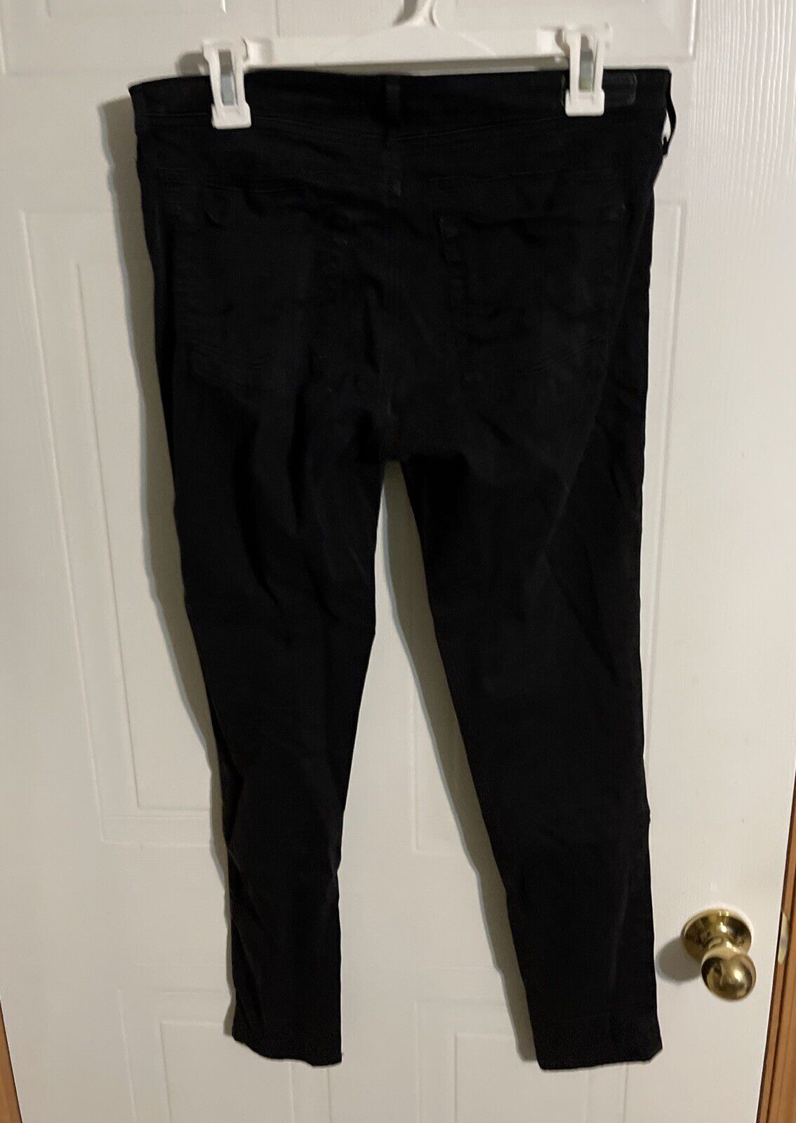 Black Adriano Goldschmied Abbey Ankle jeans hanging on a white hanger against a white door