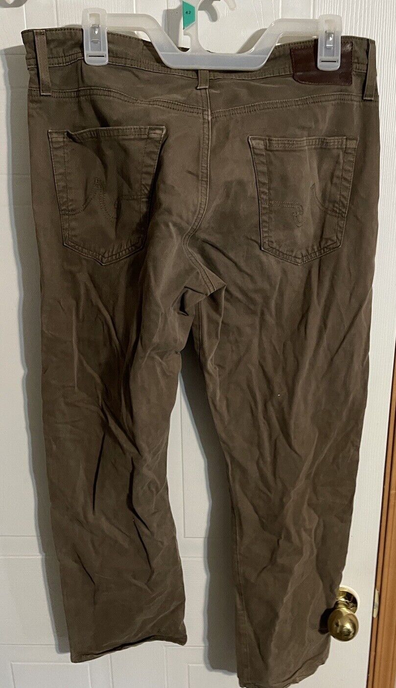 Brown AG The Graduate men's jeans hanging on a white hanger showing back pockets and belt loops