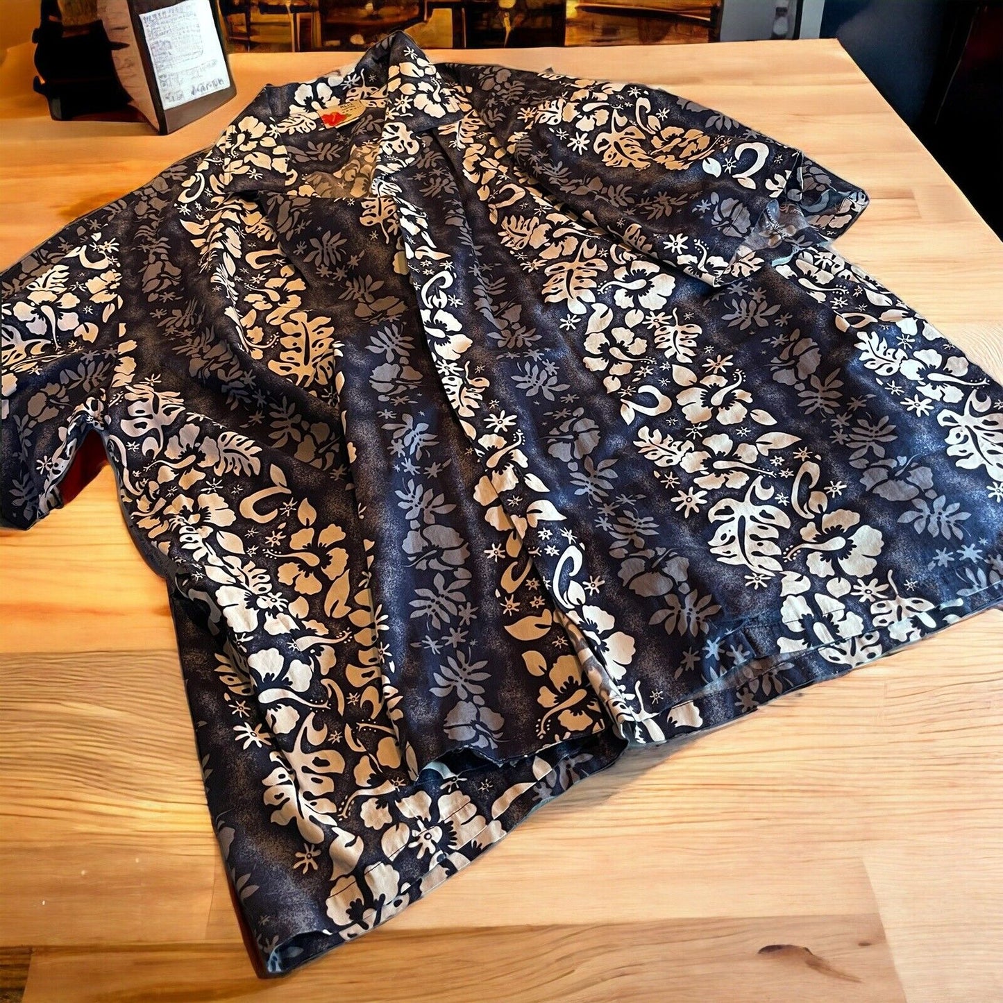 Black and white floral Ali’i Hawaiian shirt for men laid flat on wooden surface
