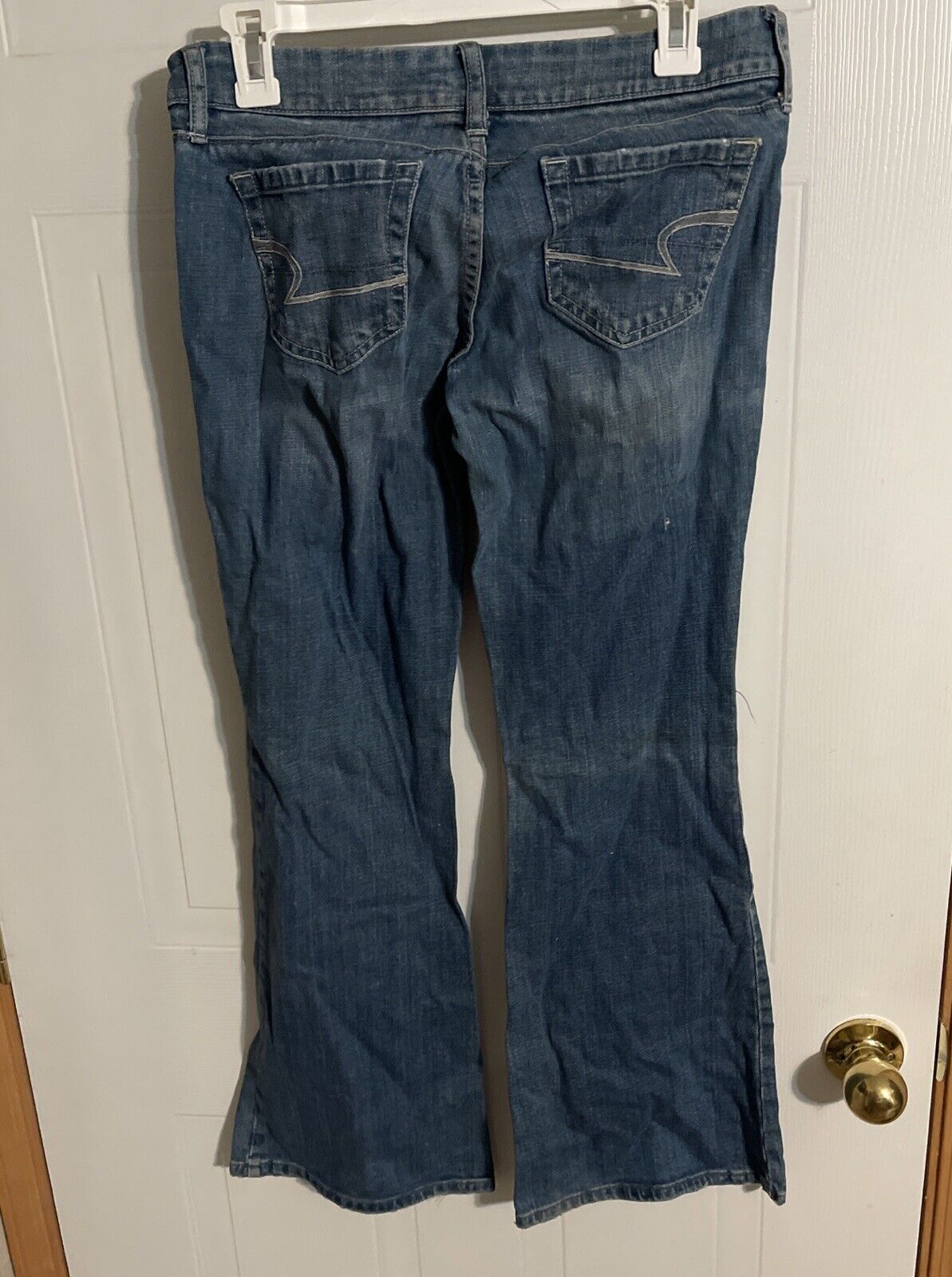 Back view of American Eagle flare jeans in dark denim hanging on a white door