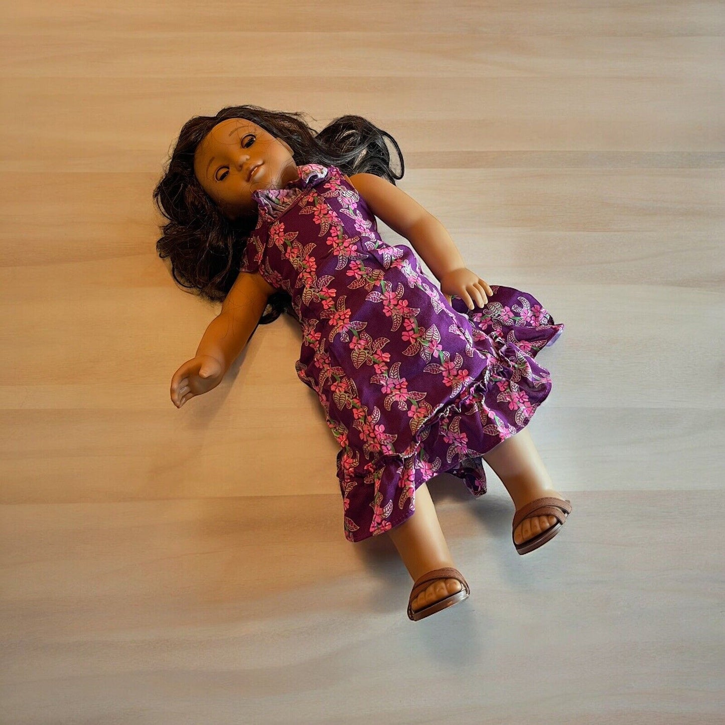 American Girl doll for sale wearing purple floral dress and brown sandals lying on wooden surface