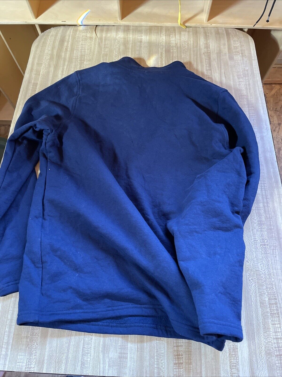 Blue American Roots quarter zip pullover laid flat on a wooden surface showing the back side