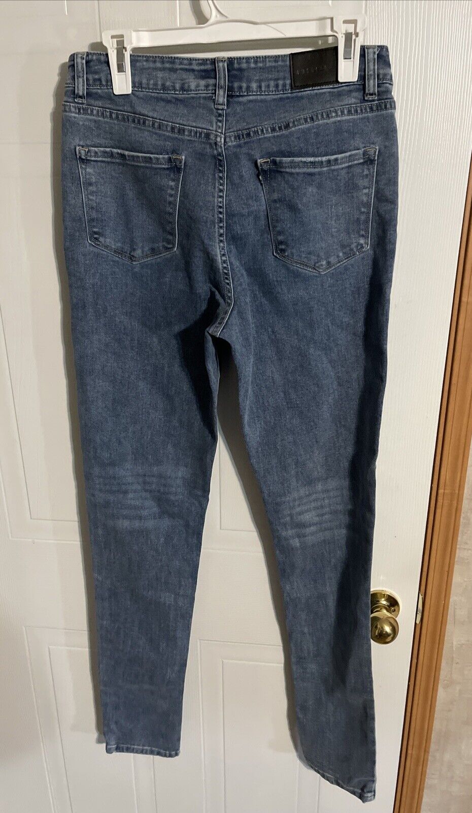 Back view of American Tall denim jeans in classic blue wash hanging on a white hanger
