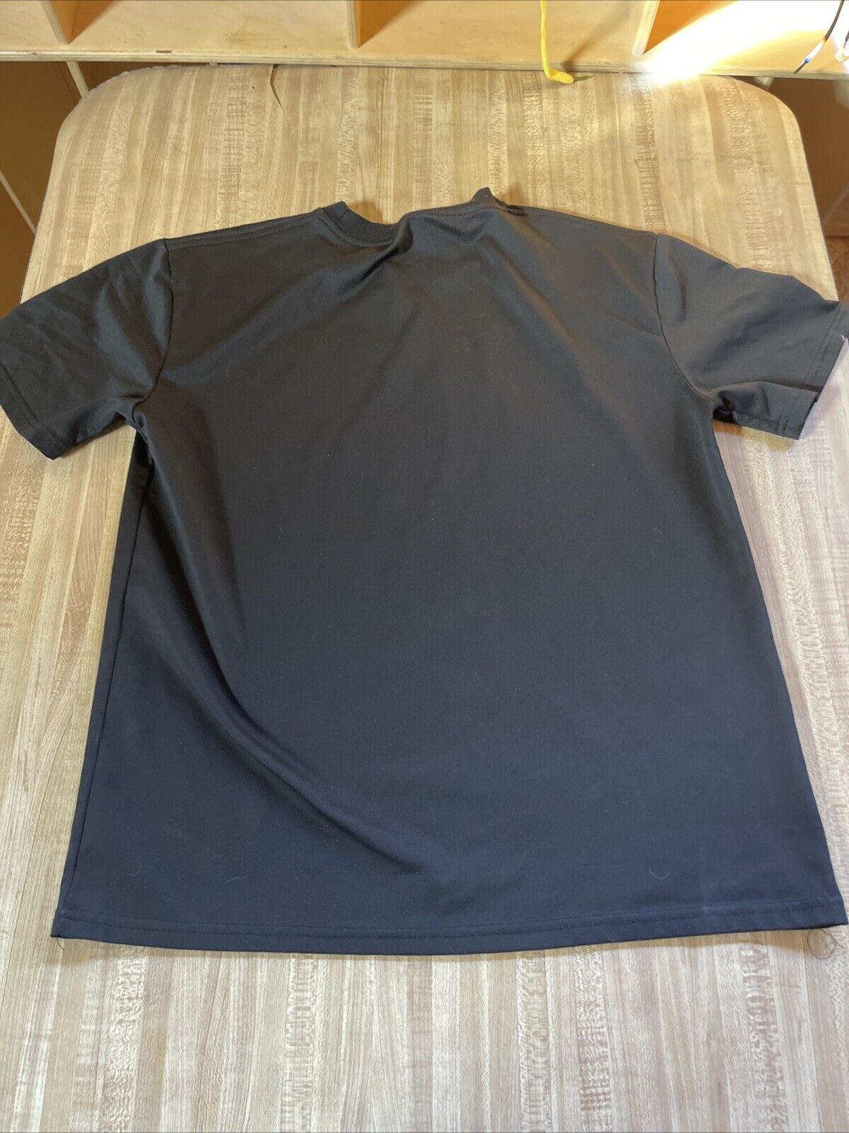 Plain black anime t shirt large size laid flat showing back side on wooden surface