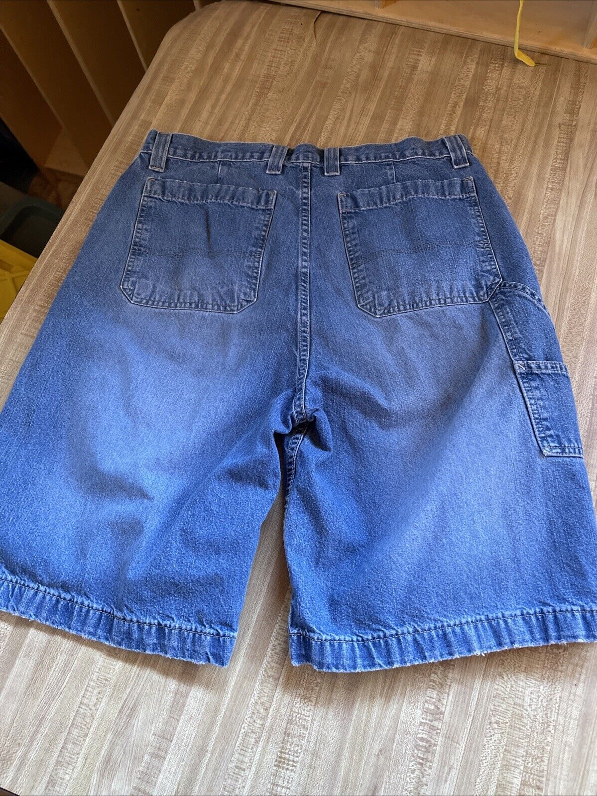 Back view of blue denim Arizona carpenter jorts 36 with belt loops and back pockets on wooden surface
