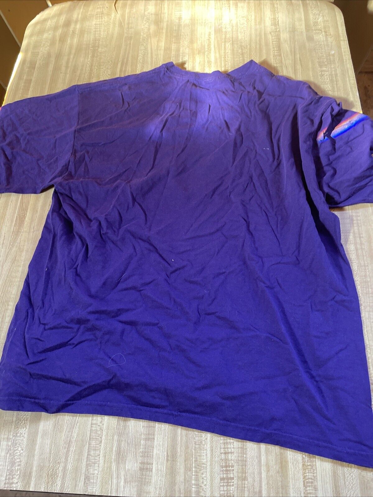 Purple As The Days Die band shirt laid flat on wooden surface showing back side with creases