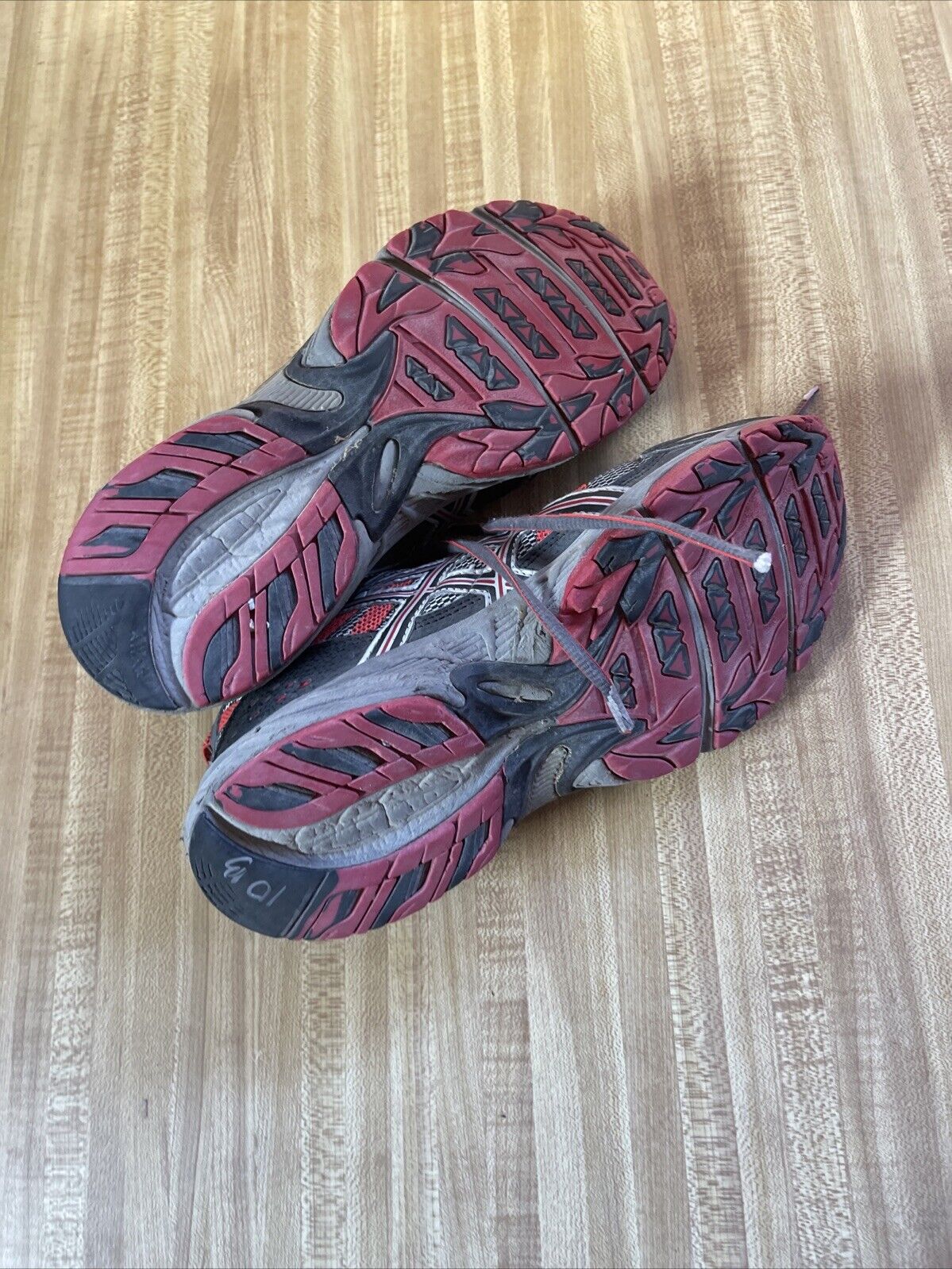 Worn ASICS Gel Venture 4 men’s size 12 trail running shoes with red and black soles on wooden floor