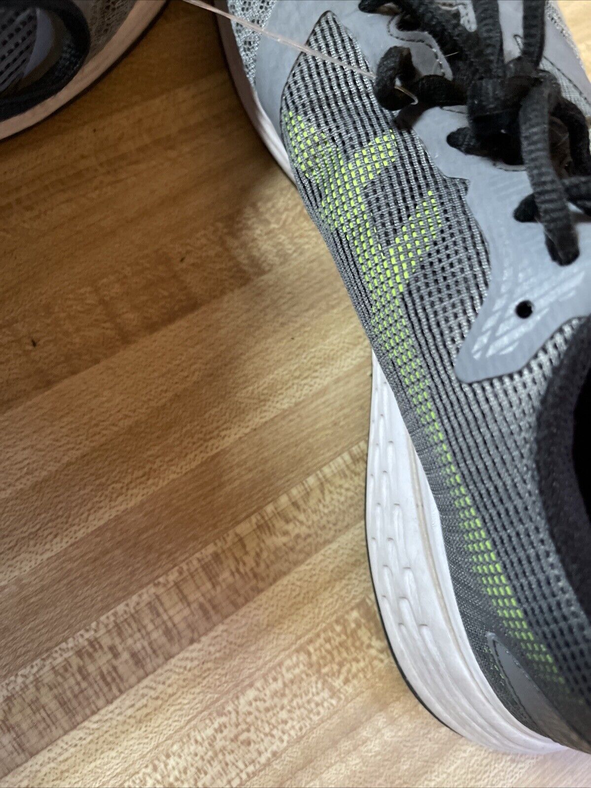 Close-up of ASICS Patriot 10 men’s running shoes in gray and green on wooden floor