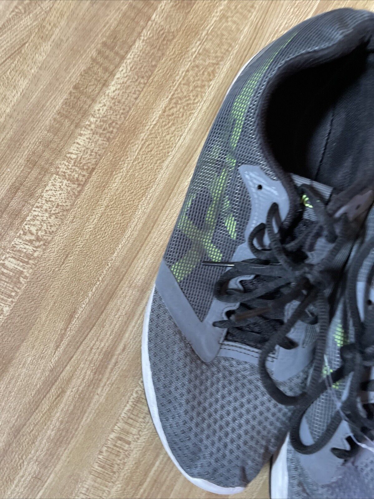 Gray and green ASICS Patriot 10 men’s running shoes on wooden floor with black laces