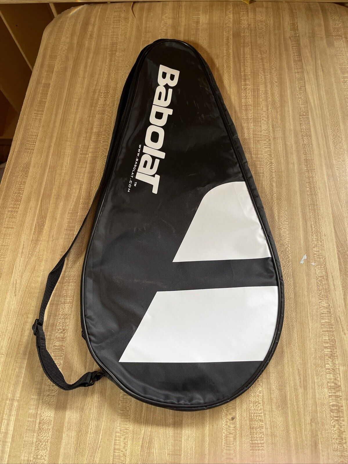 Black Babolat racquet cover with strap featuring white logo and geometric design on wooden surface