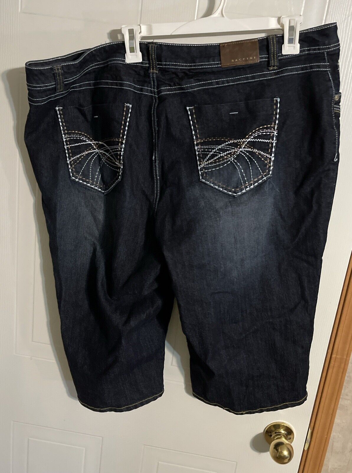 Baccini plus size denim jorts in dark wash with decorative back pocket stitching hanging on a white hanger