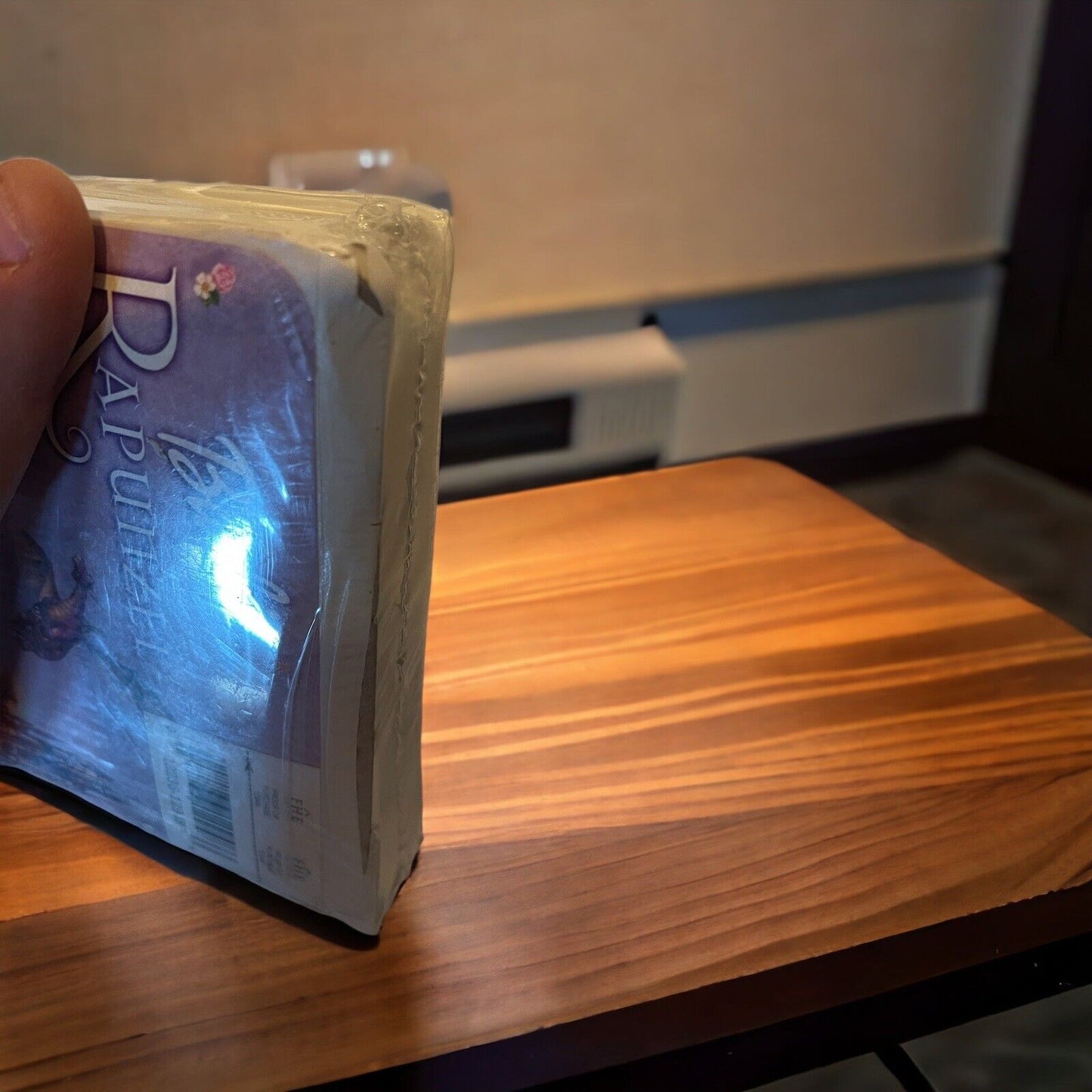 Hand holding a sealed Barbie as Rapunzel VHS tape with a purple cover on a wooden table