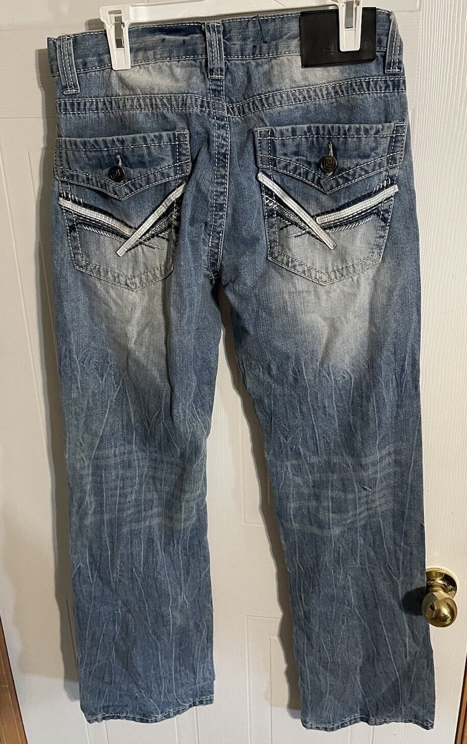 Blue denim jeans with back pockets featuring white stitch accents hanging on clip hanger