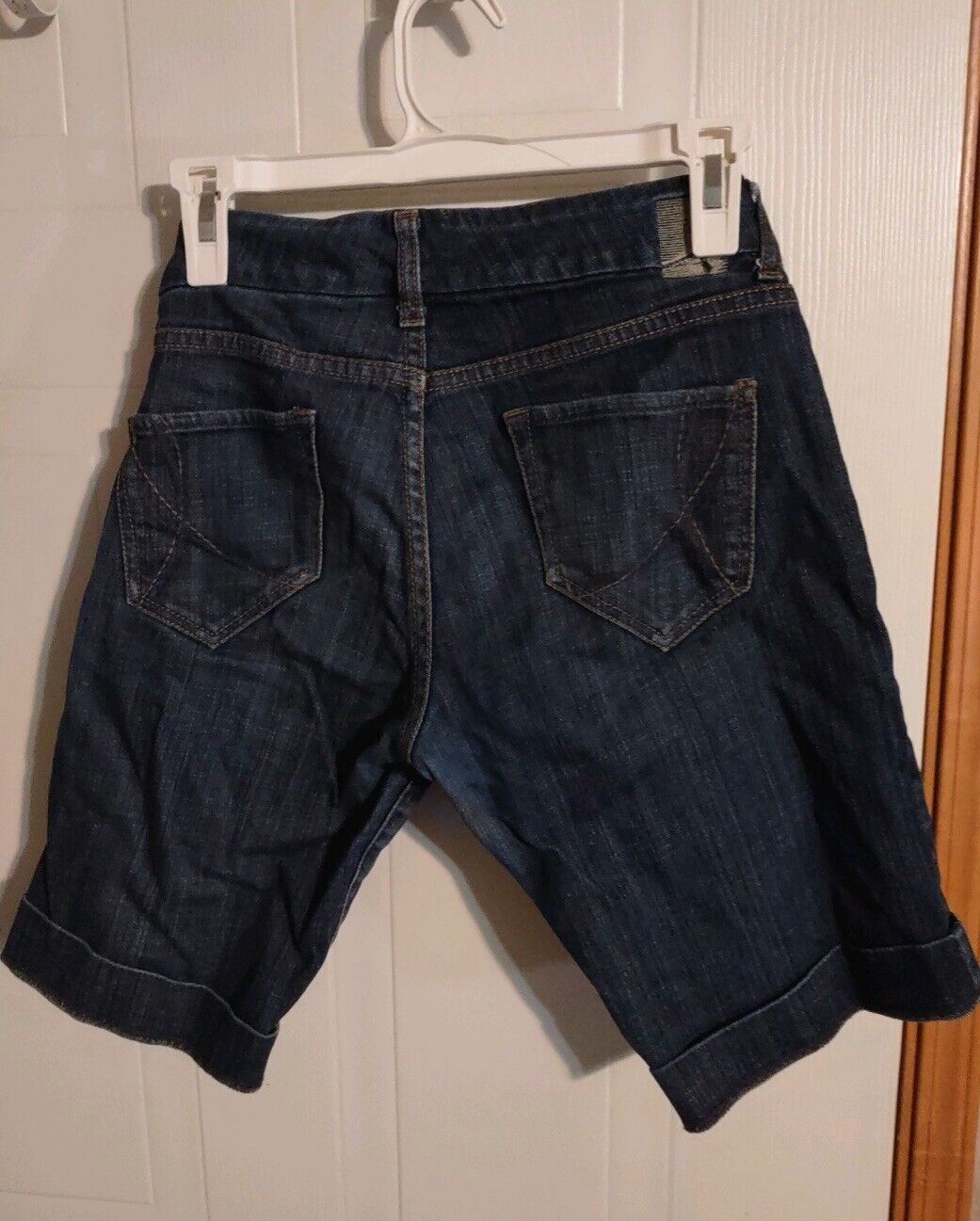 Dark denim size 28 Bermuda shorts hanging on a white hanger with back pockets visible