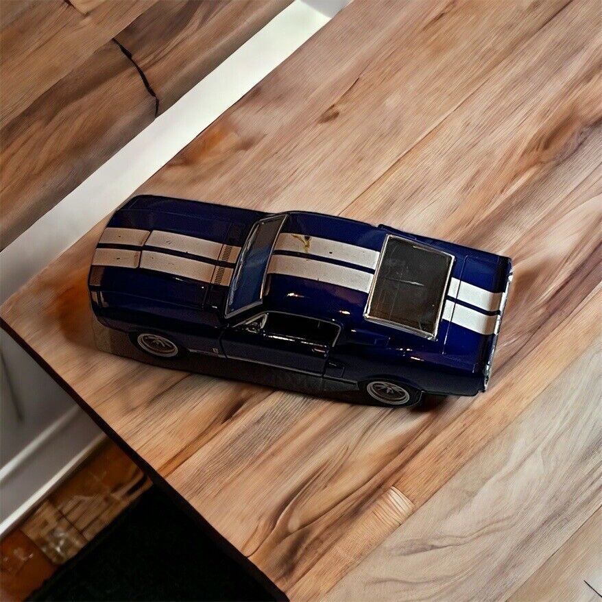 Blue diecast muscle car model with white racing stripes on wooden surface by 1118 Emporium