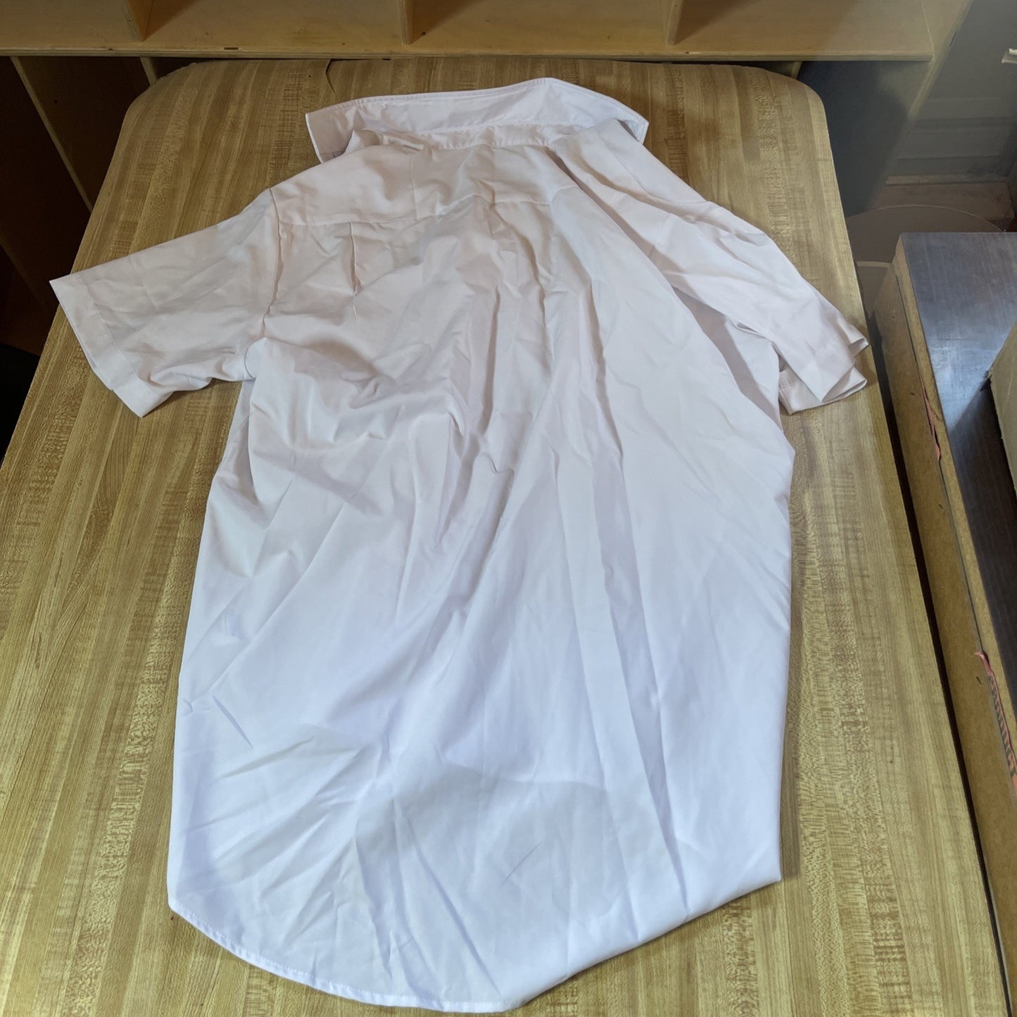 White men's athletic button up shirt laid flat on a wooden surface showing back side