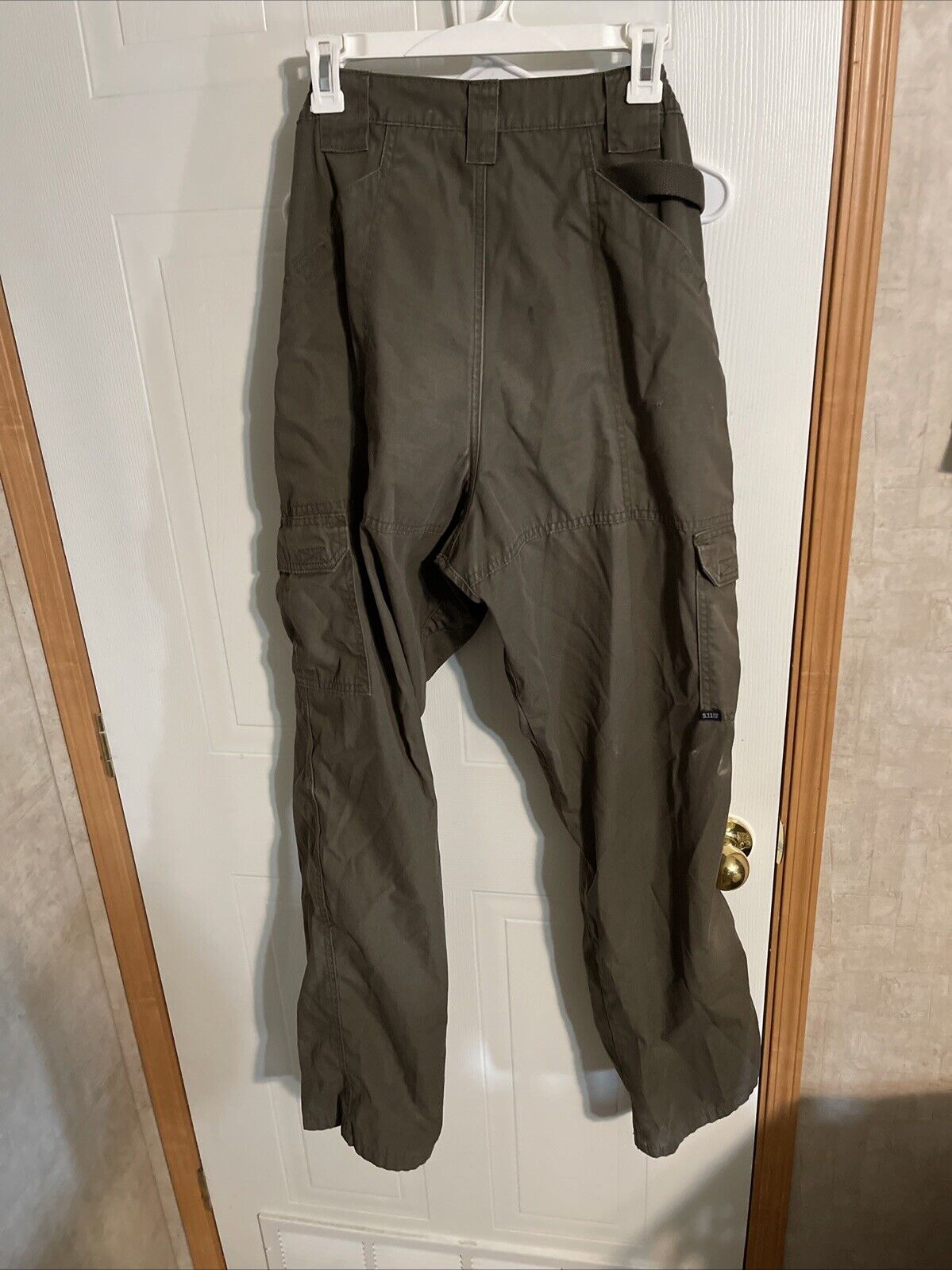 Men's tactical cargo pants in olive green hanging on white hanger against door background