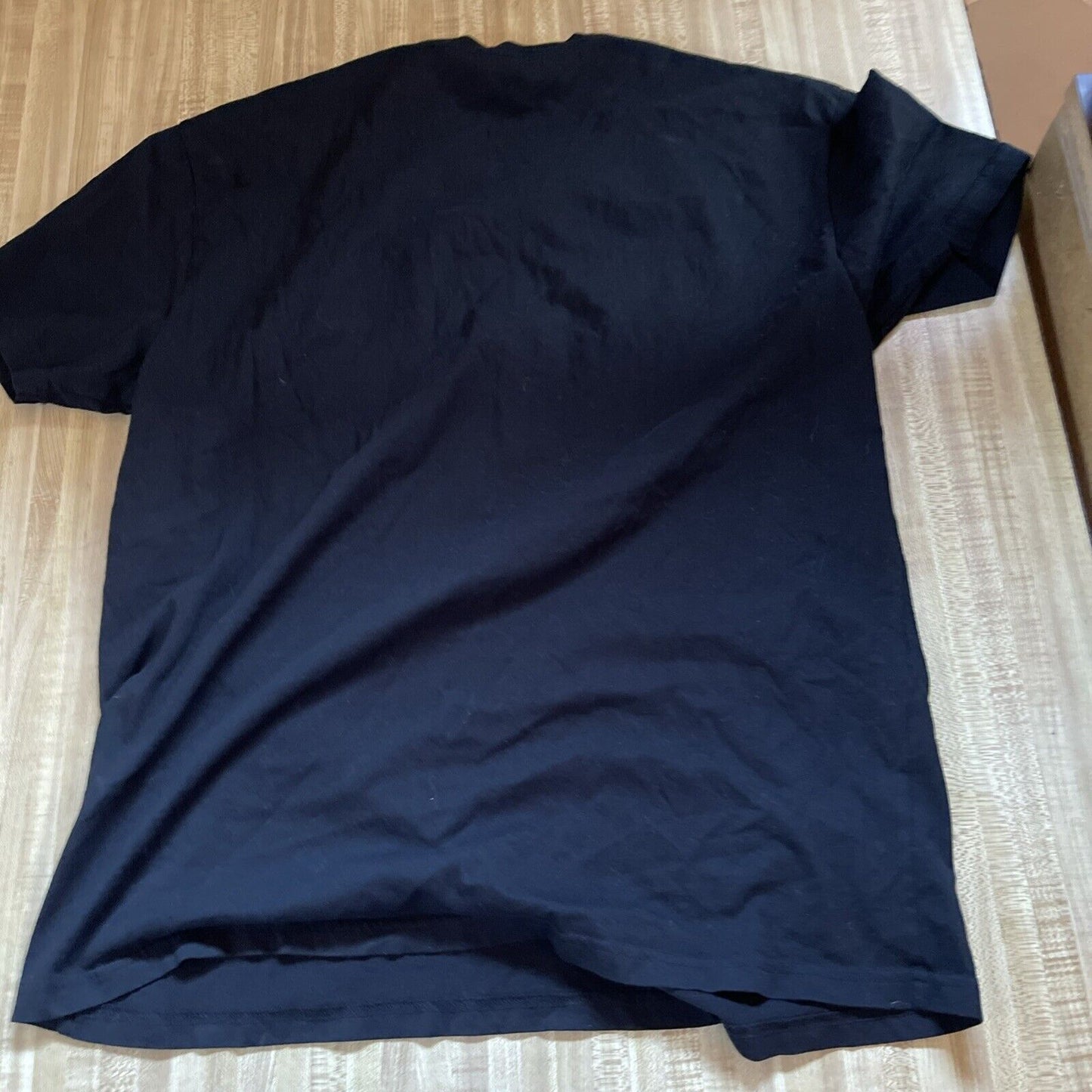 Black plain t-shirt laid flat on wooden surface for Qmx Firefly merchandise