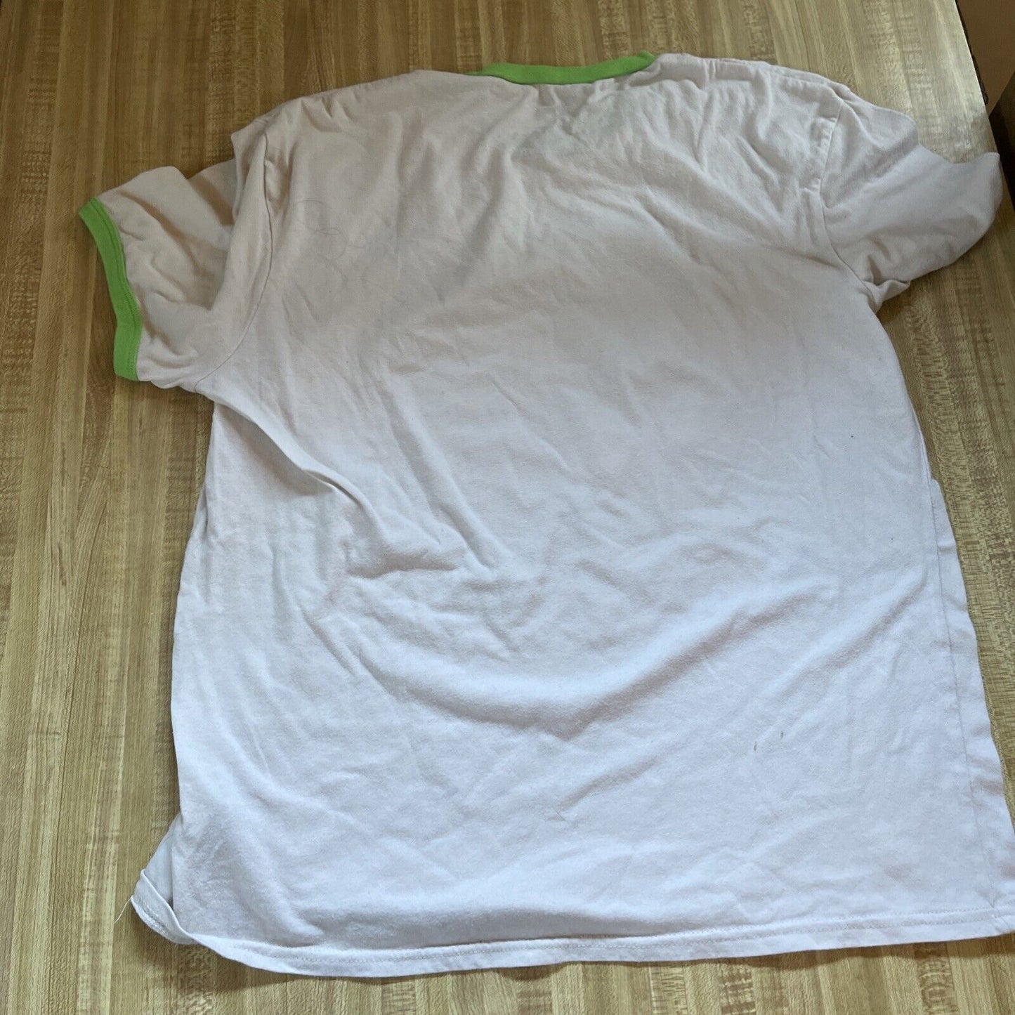 White Rick and Morty ringer t shirt with green collar and sleeve edges laid flat on wooden surface