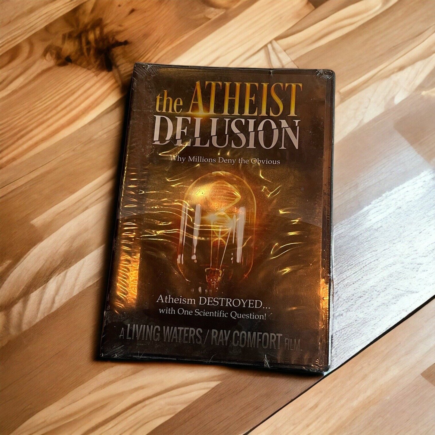 The Atheist Delusion DVD by 1118 Emporium with cover showing a glowing light bulb on wooden surface