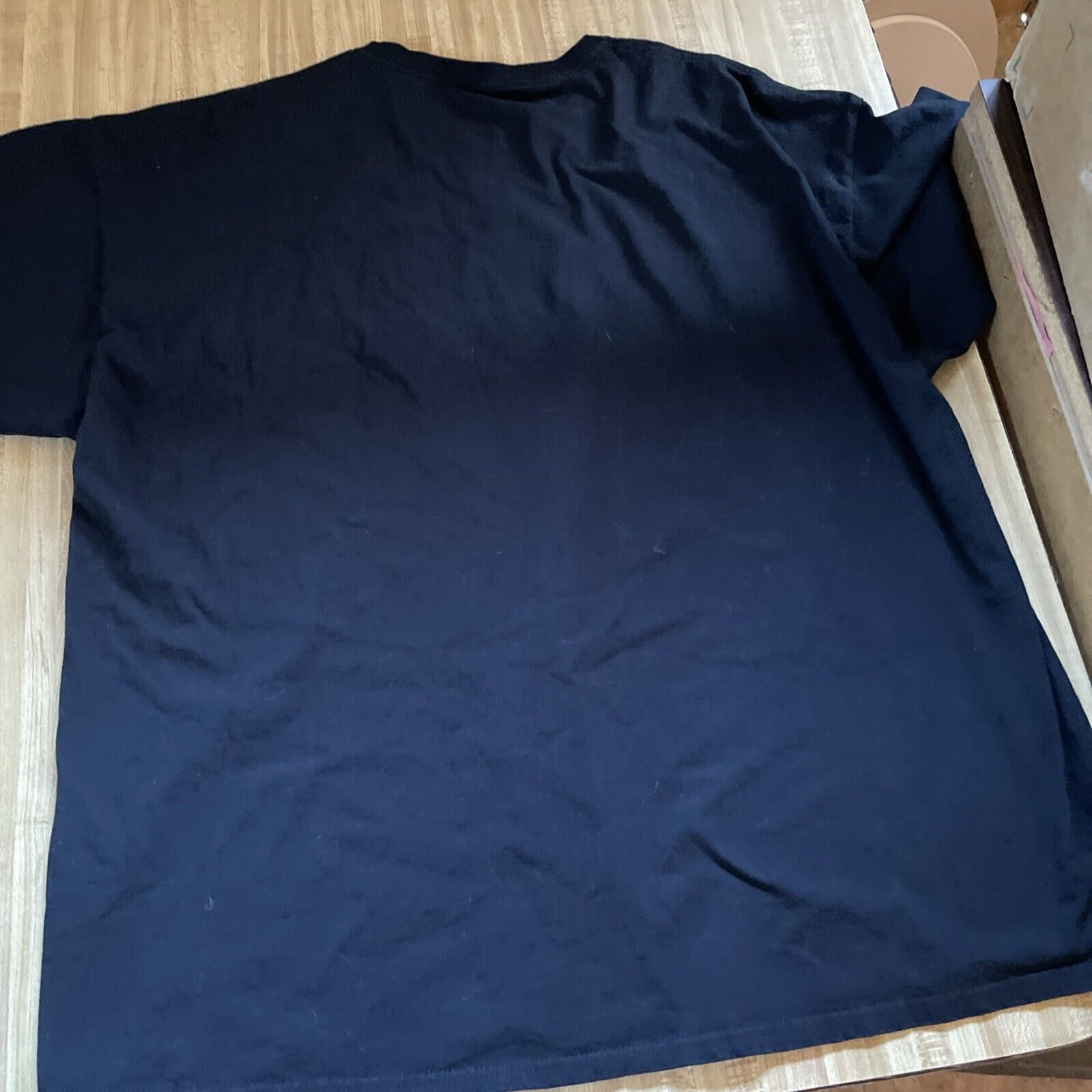 Black plain back view of horror fan gift shirt 3XL laid flat on wooden surface