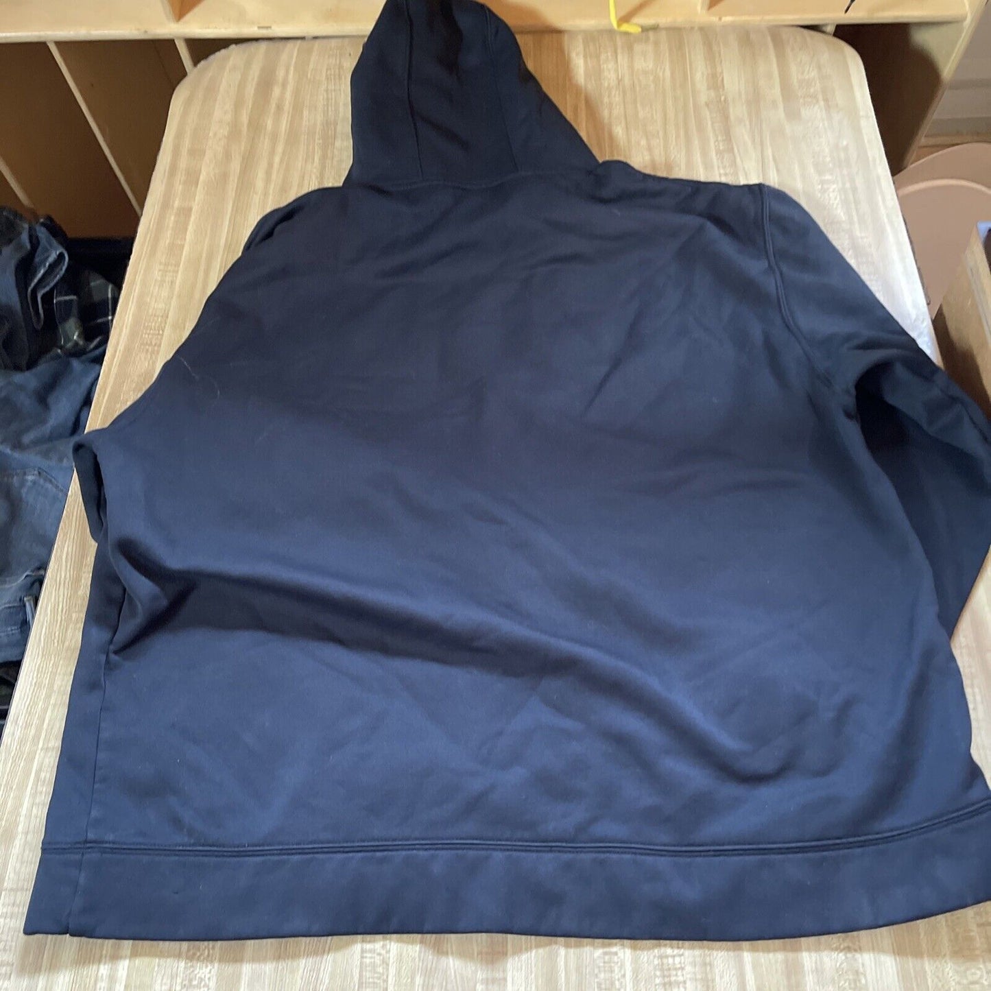 Back view of black Under Armour pullover hoodie laid flat on a beige surface from 1118 Emporium