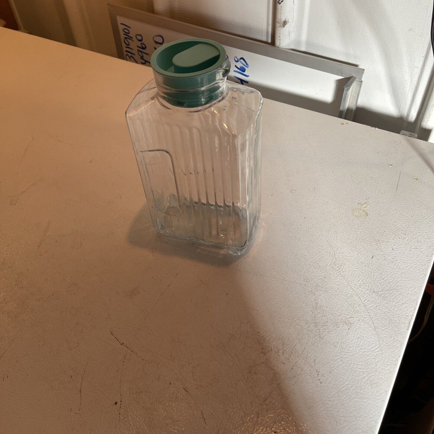 Clear vintage glass refrigerator pitcher with green lid on a white surface