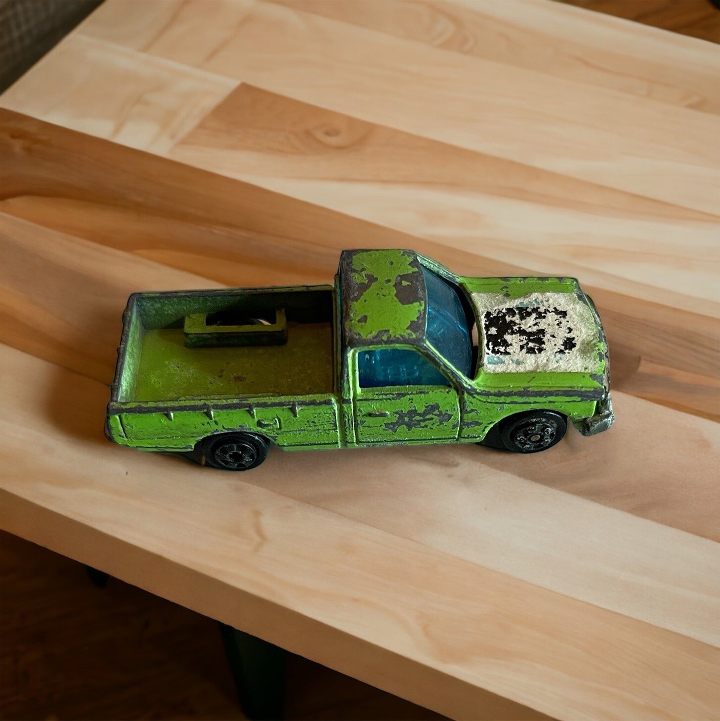 Vintage Zylmex Datsun pickup toy in green with worn paint on a wooden surface
