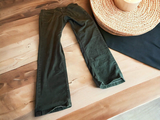 Dark green 5.11 tactical jeans for men laid flat on wooden surface next to straw hat