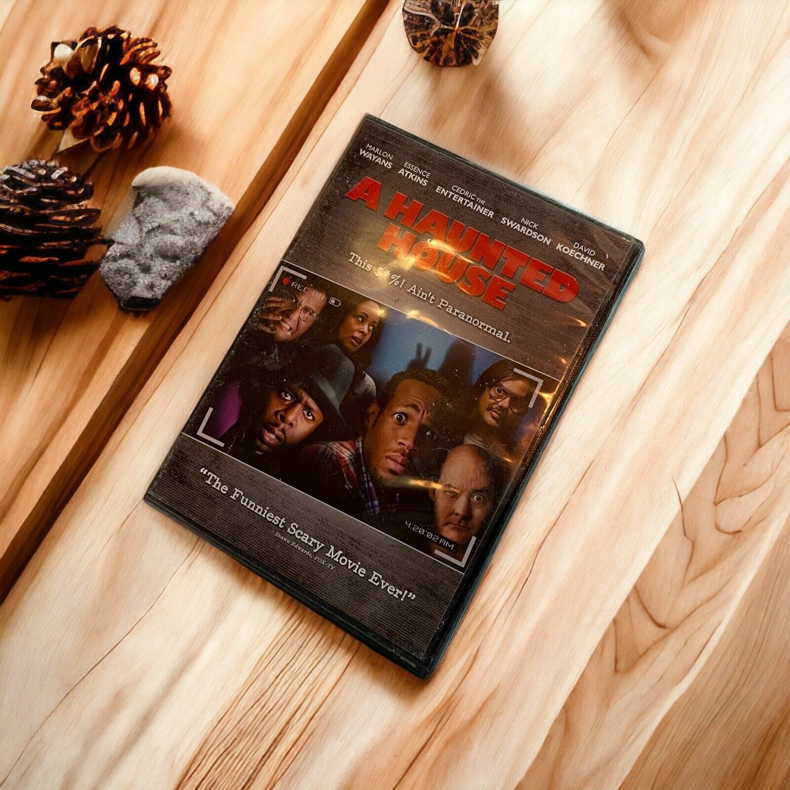A Haunted House DVD case on a wooden surface with pine cones and natural decor