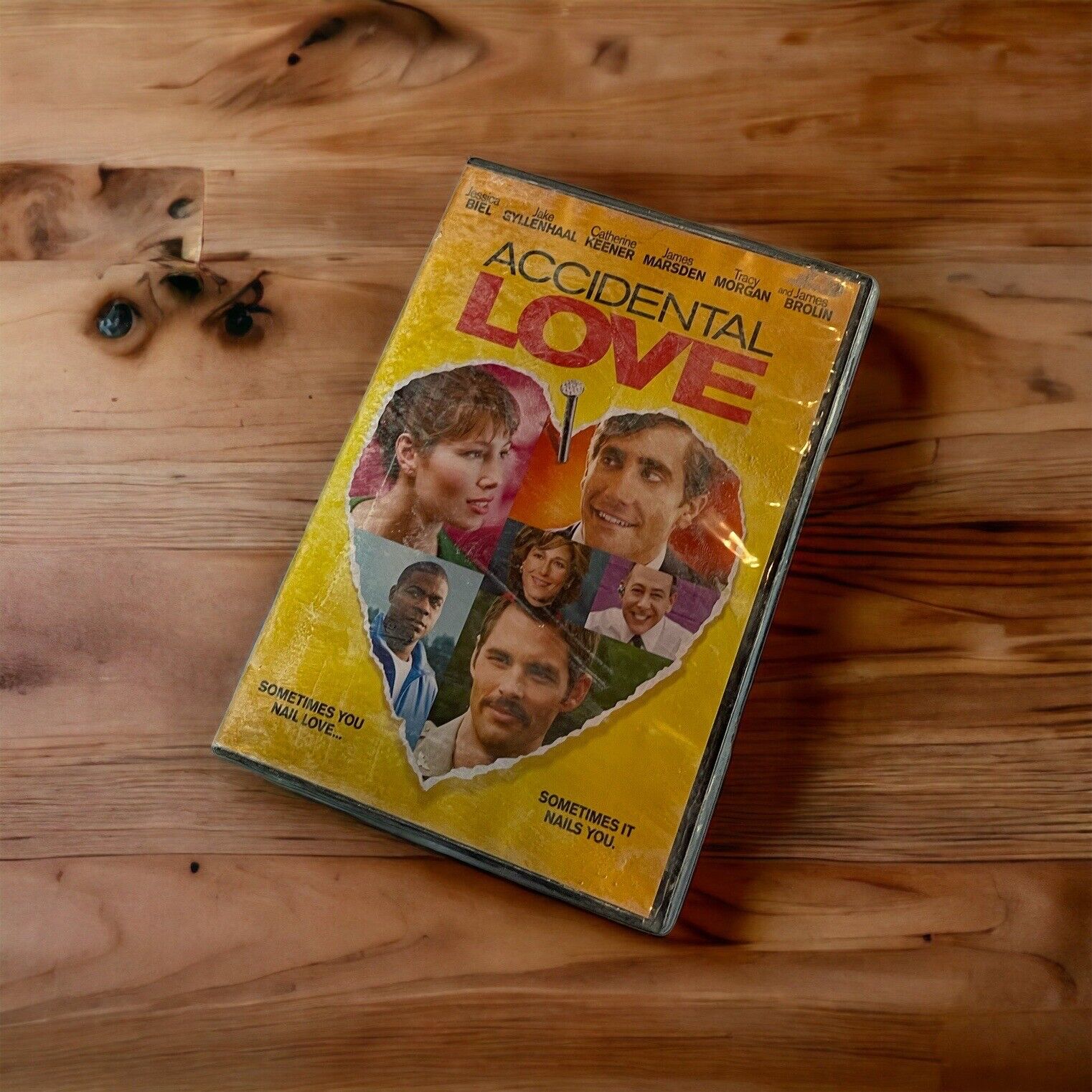 Accidental Love DVD with yellow cover featuring a torn heart and cast photos on wooden surface