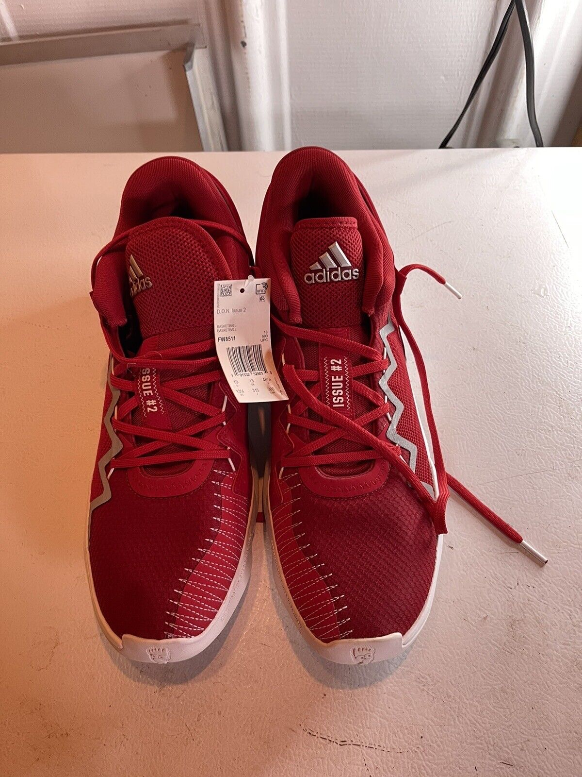 Red adidas d.o.n. issue 2 size 13.5 basketball shoes with white accents and laces on a beige surface