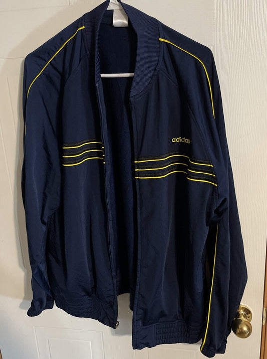 Adidas track jacket large in navy blue with yellow stripes hanging on a white hanger