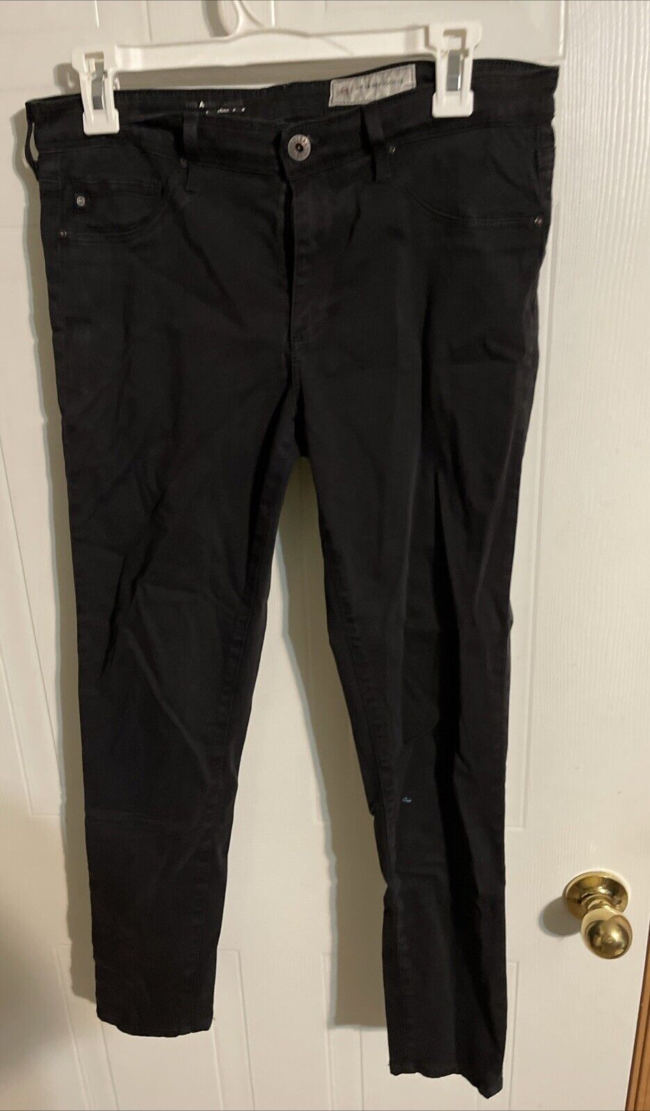 Black Adriano Goldschmied Abbey Ankle jeans hanging on white hanger against door