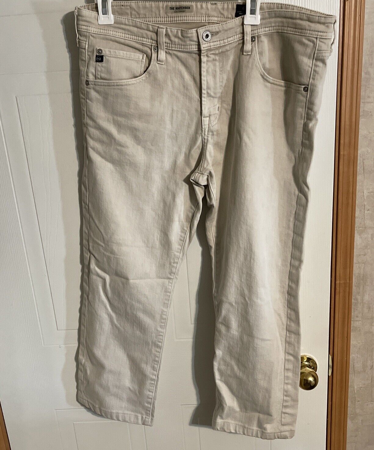 Beige Adriano Goldschmied Matchbox jeans hanging on white door with front pockets and button closure