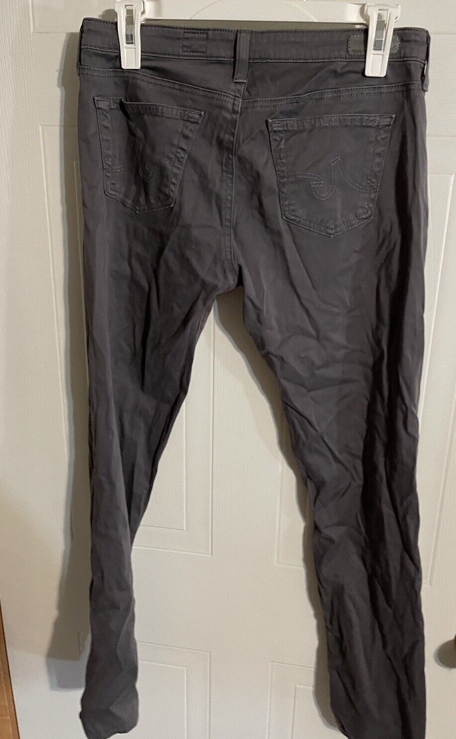 Back view of black Adriano Goldschmied women's jeans hanging on clips against white door