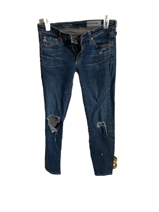 Distressed dark wash AG legging ankle jeans with front and knee rips hanging on white clips