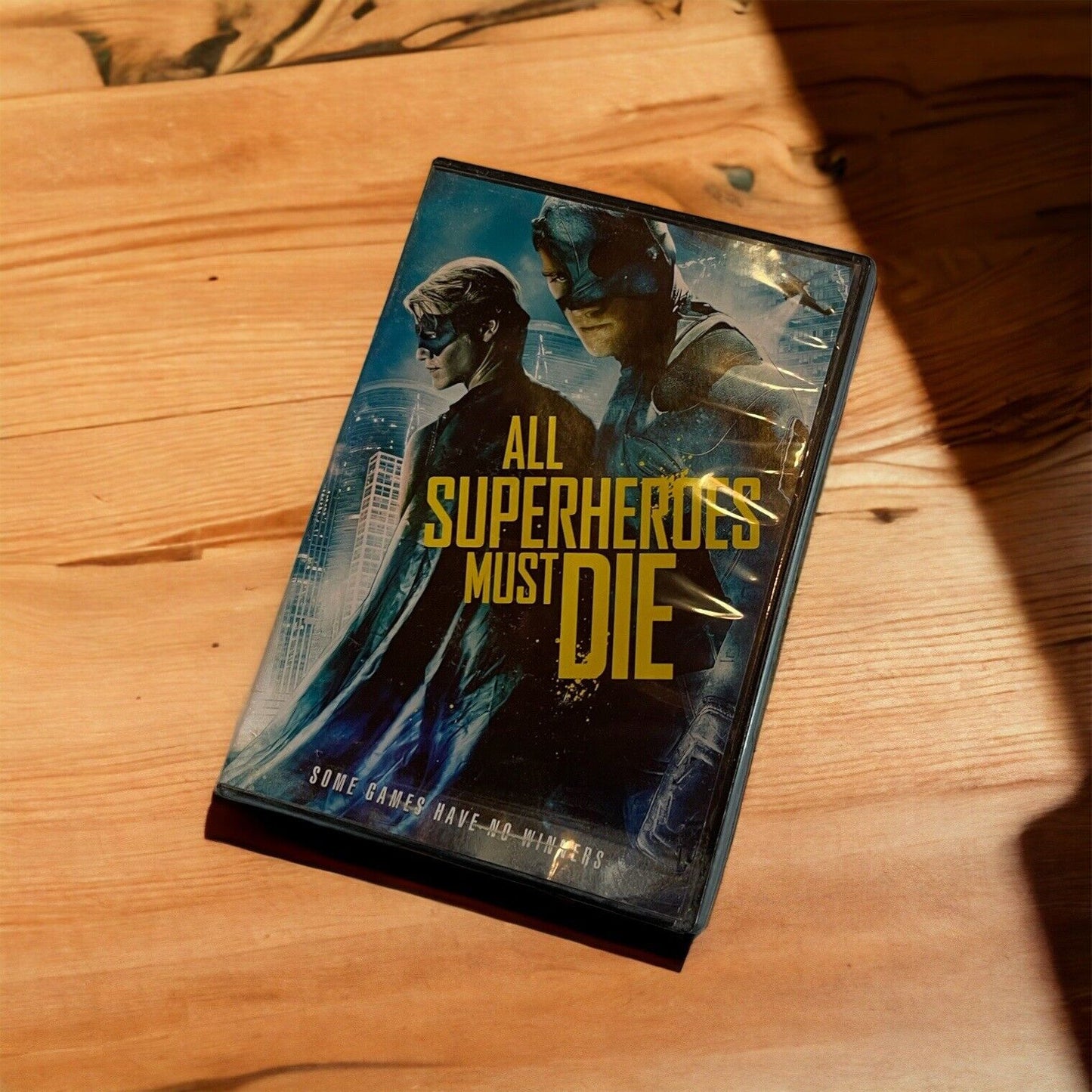 All Superheroes Must Die DVD with superhero characters on cover placed on wooden surface