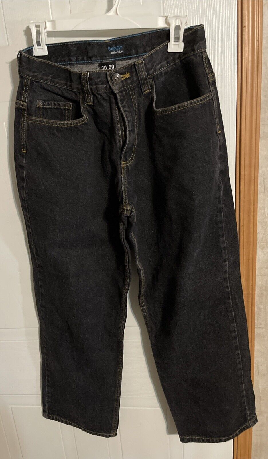 Anchor Blue baggy jeans in black hanging on white clip hanger against door background