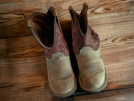 Aged Ariat Fatbaby Heritage boots with brown leather upper and worn beige toe on wooden floor