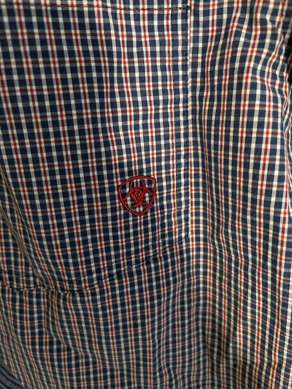 Close-up of Ariat Pro Series shirt with red and navy blue plaid pattern and Ariat logo embroidery