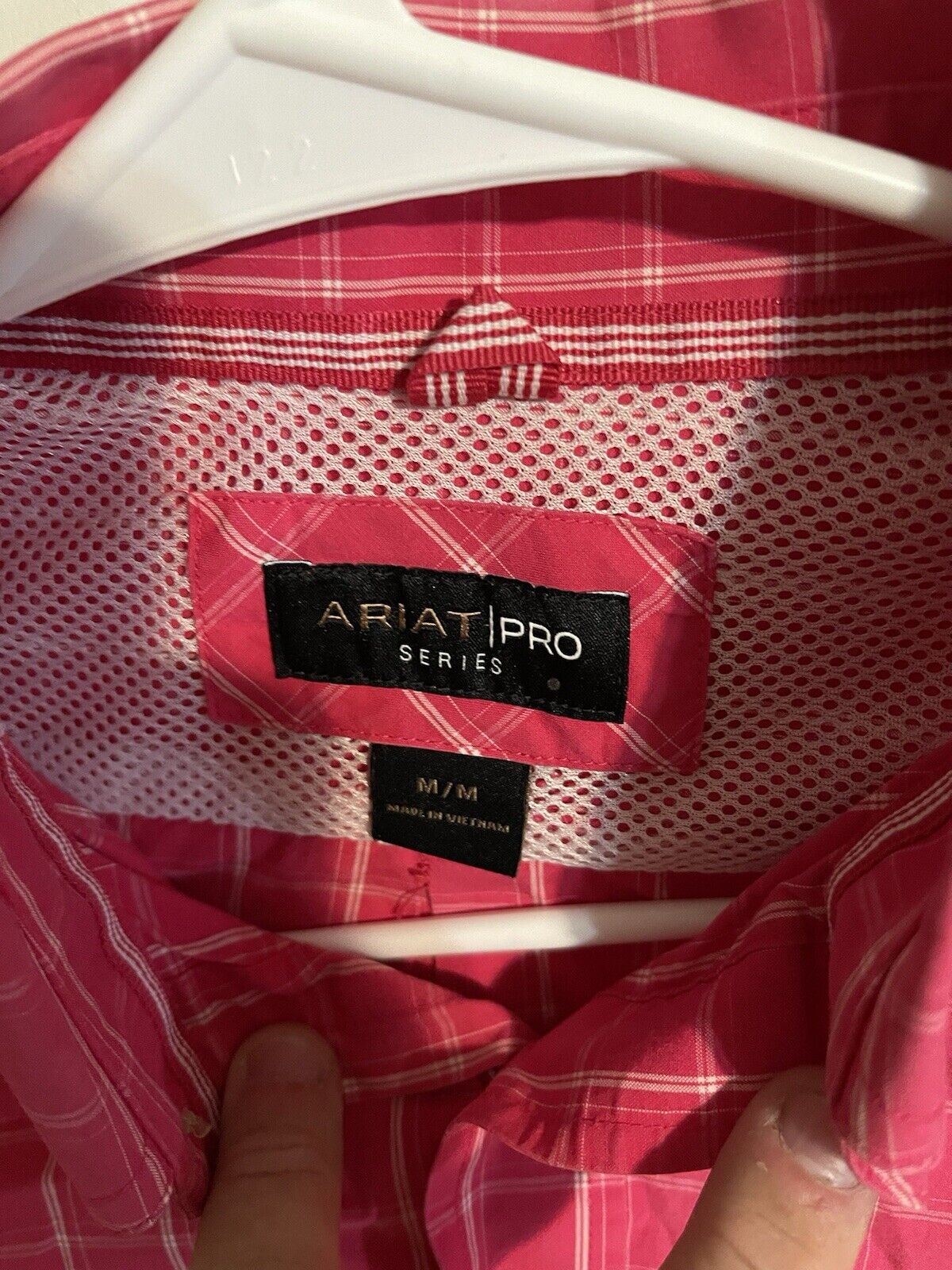 Close-up of Ariat Pro Series shirt label inside pink plaid shirt on white hanger