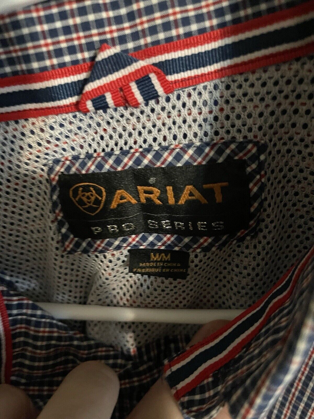Close-up of Ariat Pro Series shirt label with plaid trim and breathable mesh fabric