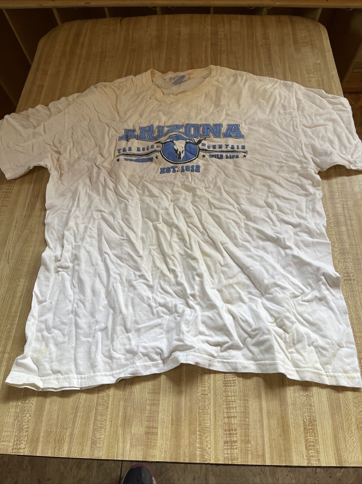 White Arizona tourist shirt XL with blue text and graphic laid flat on wooden surface