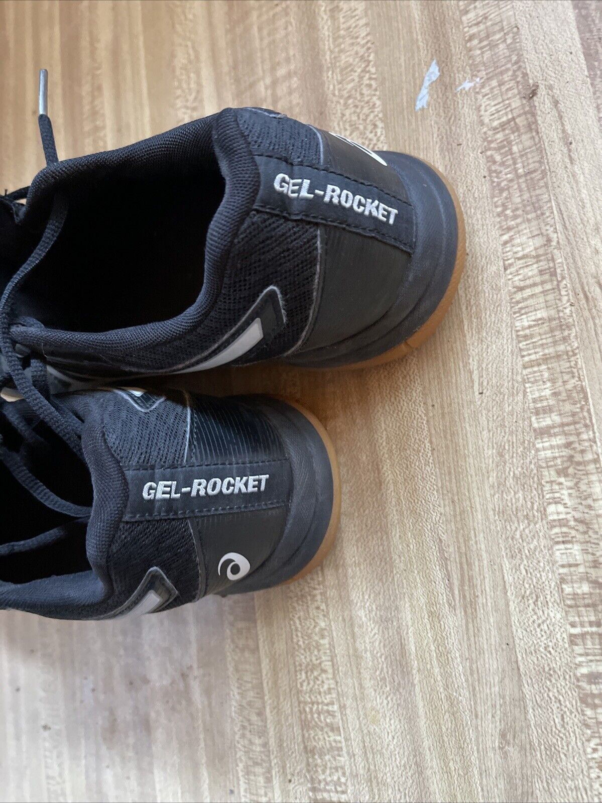 Black ASICS Gel Rocket size 9.5 shoes showing heel area with logo on wooden floor